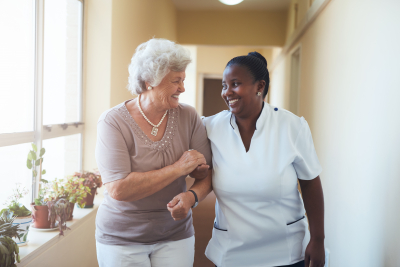 portrait of happy female caregiver and senior women walking together at home